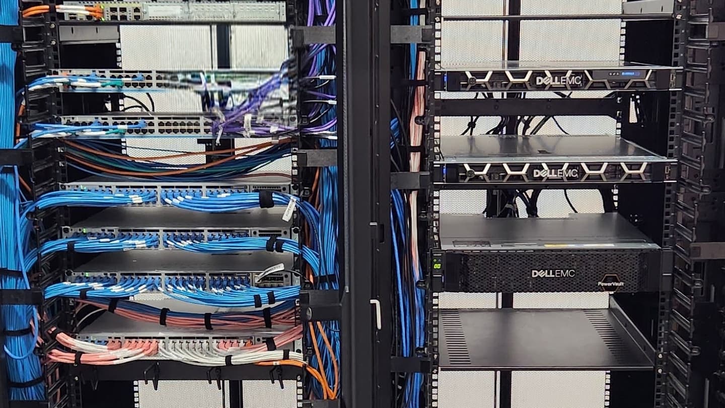 Two Dell EMC PowerEdge servers and a Dell EMC PowerVault storage array installed in a server rack, beside patch panels and network switches